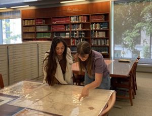 Two women are looking at maps laid on a table.