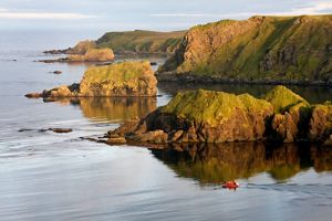 A small red dinghy is dwarfed by the rocky shoreline of Hawadax Island.