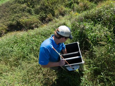 A person interacts with a drain water management system in a field.