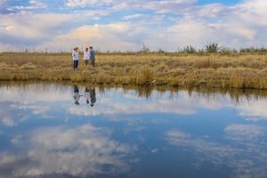 Three men stand on the edge of a pond.