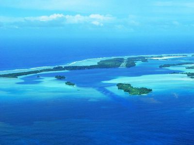 Aerial view of an atoll with patches of green forests and sand.