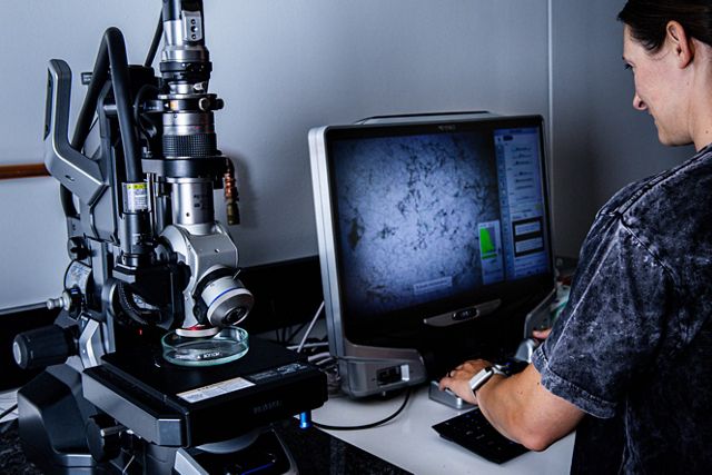 A person looks under a microscope at microfibers. 