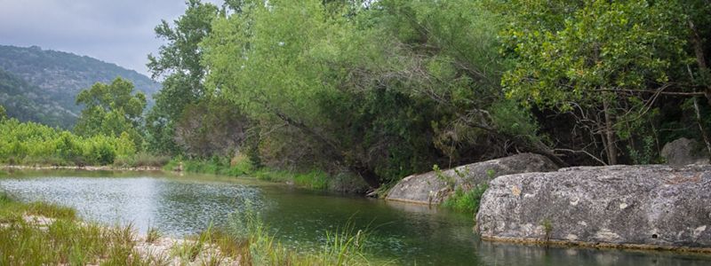 A green river lined with rocks and foliage.