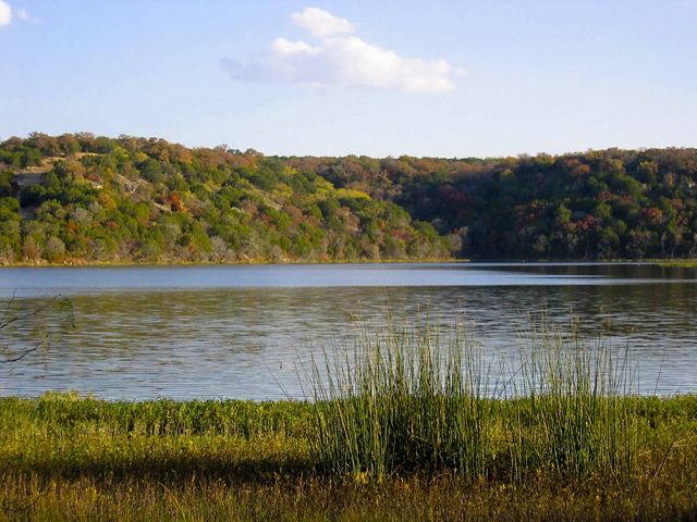 Un lago en primer plano con una cadena de colinas verdes detrás debajo del cielo azul.