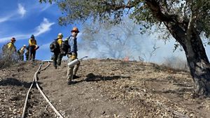 A man stands on a hill with controlled burn equipment while others stand in the background in yellow jackets.