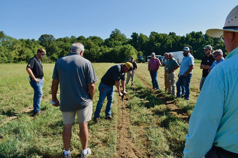 A group of people stand together in a farm field watching a demonstration of precision nutrient application best practices.