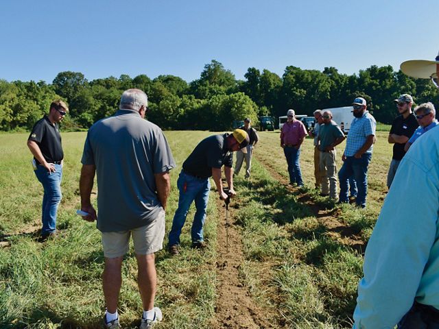 A group of people stand together in a farm field watching a demonstration of precision nutrient application best practices.