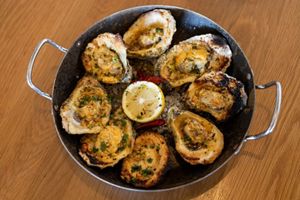 Eight grilled oysters sit on a plate with a lemon wedge.