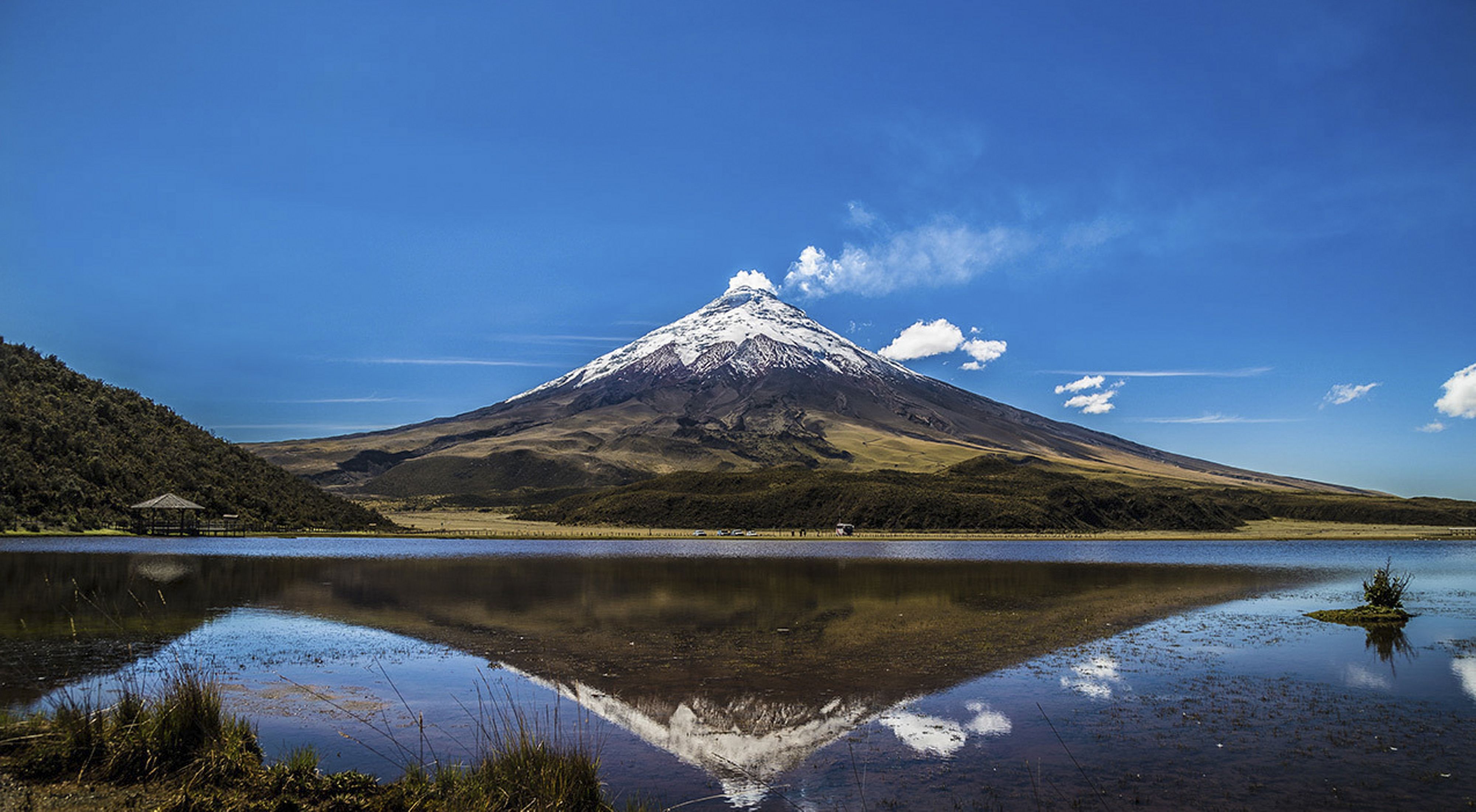 snow tipped volcano - Cotopaxi - beneath a bright blue sky and reflected in still lake water