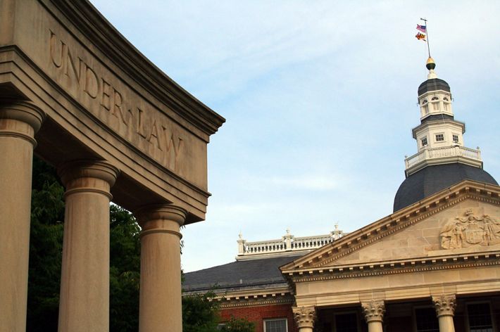 Maryland state house in Annapolis. On the left three stone columns support a plinth inscribed with the words Under Law. The domed cupola of the main statehouse building rises in the background.