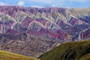 Landscape view of a mountain range with rows of pointed rock formations 'striped' with colors of purple, pink, and beige.