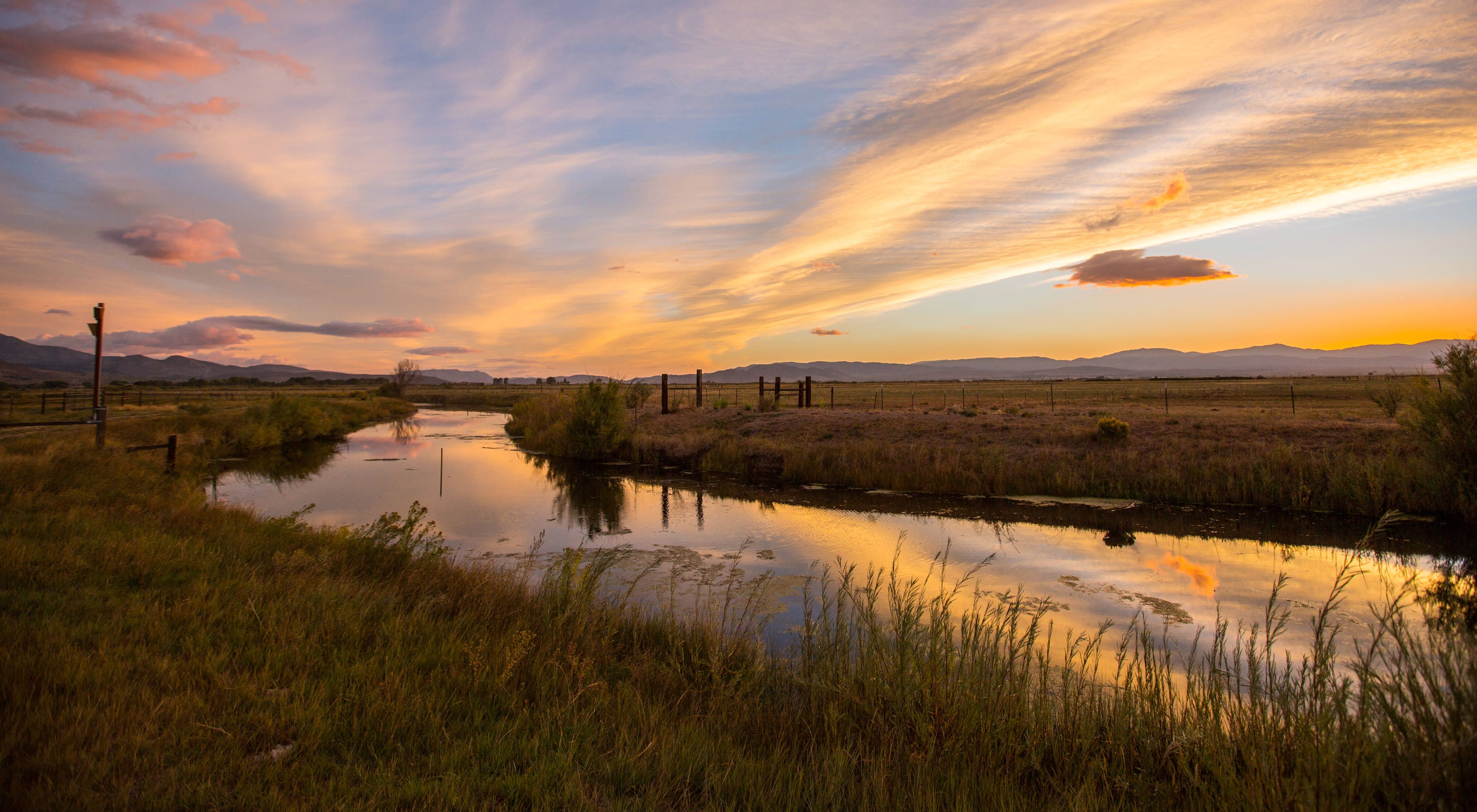 Sunset and clouds over a river running through grassy fields.