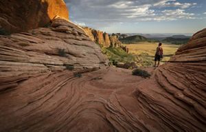 a hiker standing between two walls of layered red rock overlooking a valley.