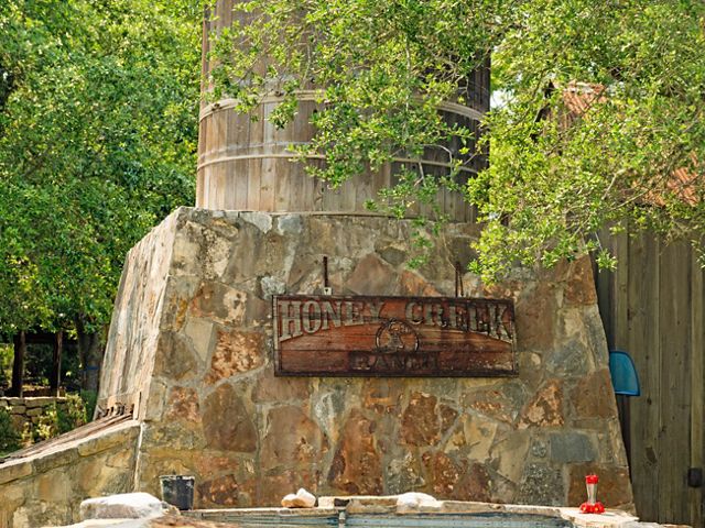 A wooden water tank surrounded by stone with a sign reading Honey Creek Ranch.
