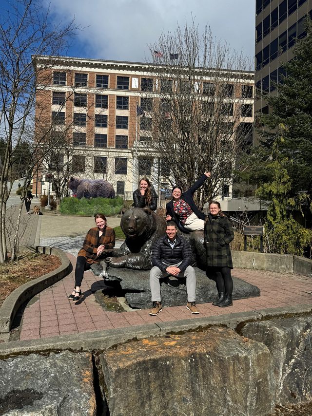 Five people pose together around a large statue of a bear.