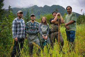 Five people standing in tall grass with mountains and fog behind them.