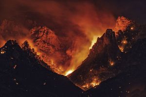 Landscape of a mountain range engulfed in a dramatic fire at night.