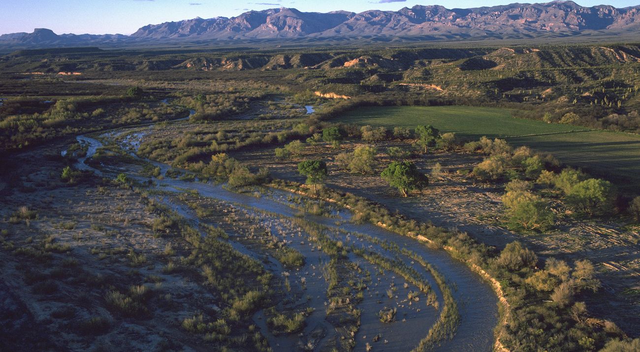 Ariel shot of a river and a green landscape with mountains in the distance.