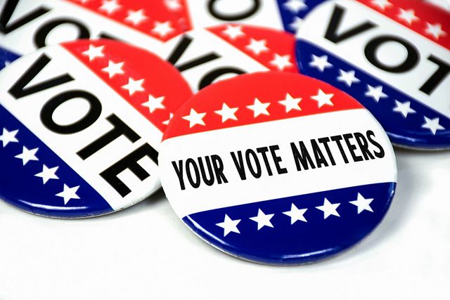 a pile of red white and blue buttons that say "Vote."