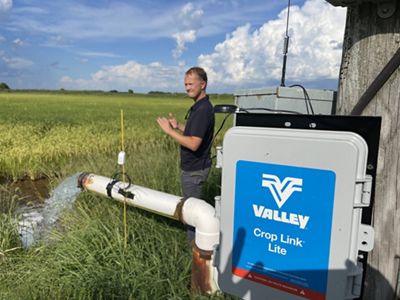 A man stands next to a well timer while water rushes out of a pipe in front of him.