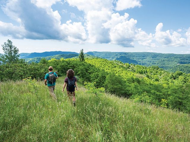 A father and son walk along a hillside trail with mountains and valley sweeping out into the distance.
