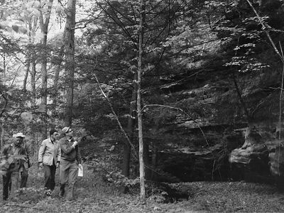 A black and white photo of three people walking through a forest. 