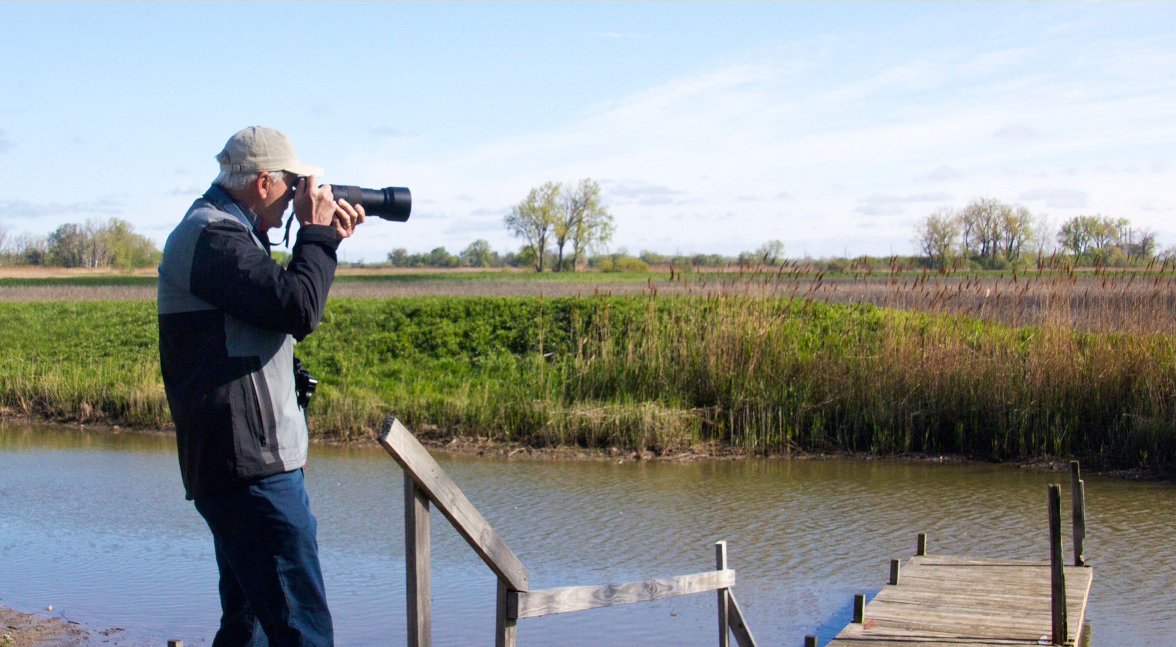 A bird watcher looks out at the still water of Erie Marsh Nature Preserve in Michigan on a cloudy day. 
