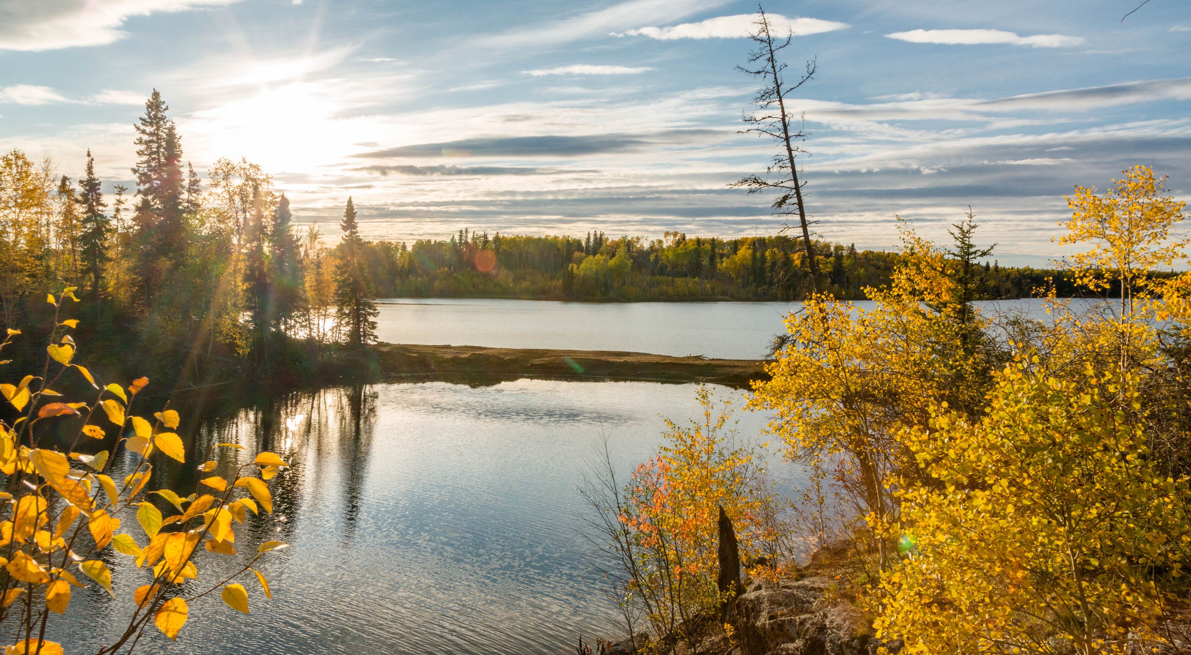View looking out over a large body of water with autumn-colored forests along its banks at sunrise.