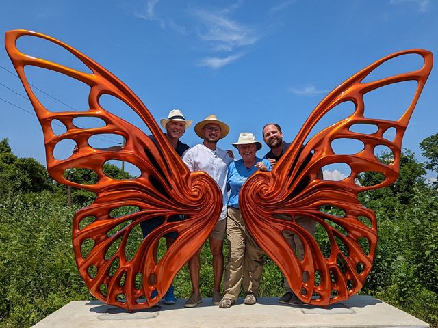 Four people posing behind a large butterfly statue. 