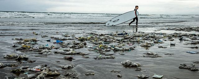 Surfer walking on beach covered in trash. 