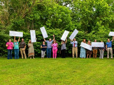 A group of people standing in green grass celebrate while holding large checks in the air.