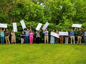 Award recipients stand on vivid green grass and in front of green trees, holding large checks.