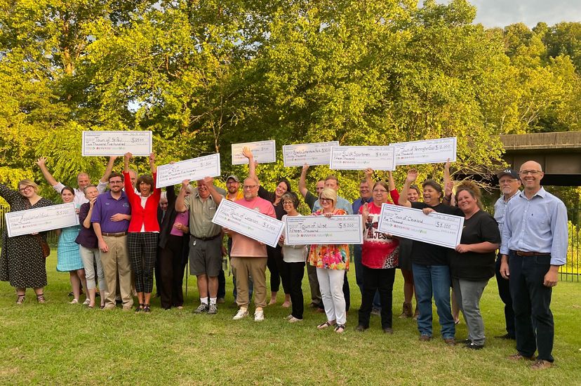 A group of people pose together, many of them holding up large novelty checks, during an event celebrating grant recipients.