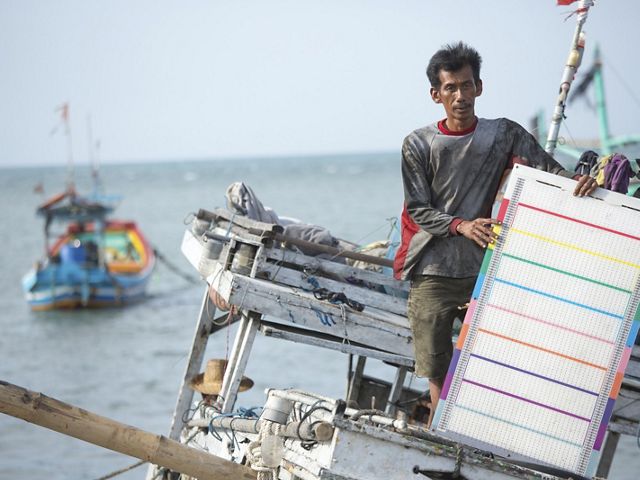 A man holds a colored board while on a boat.