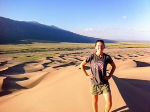 A woman standing on vast sand dunes with mountains in the background.