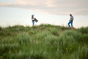 A man and a woman walking towards each other on a large grass hill.