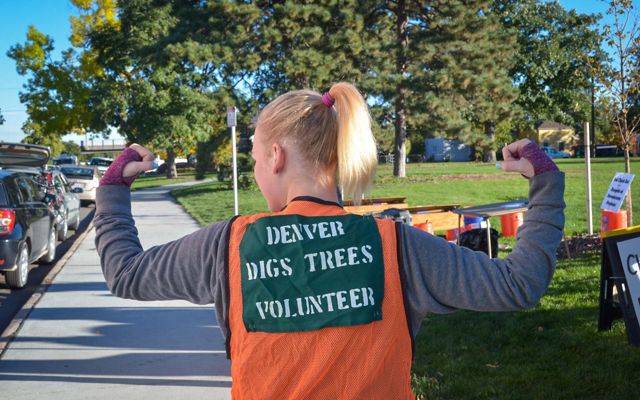 A woman flexing her arms in a orange vest at a tree planting volunteer event.