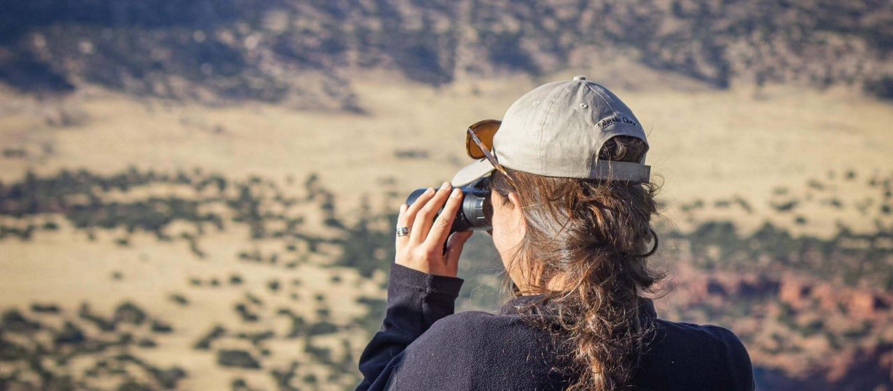 A woman looking out into a canyon through binoculars.
