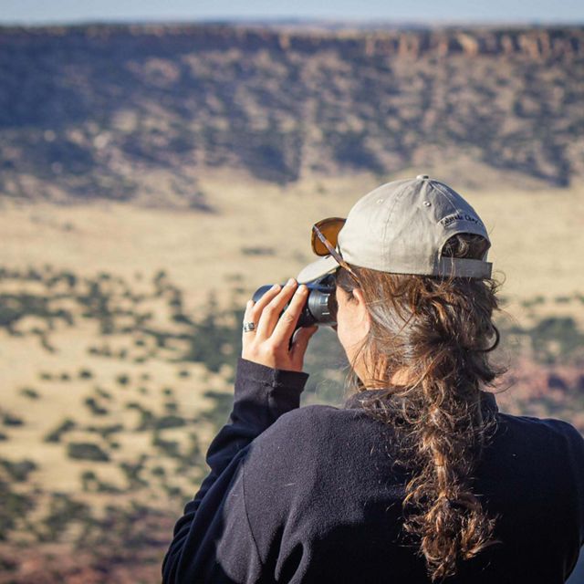 A woman looking through binoculars into a canyon.