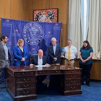 Five people standing around the governor signing a bill on a desk.