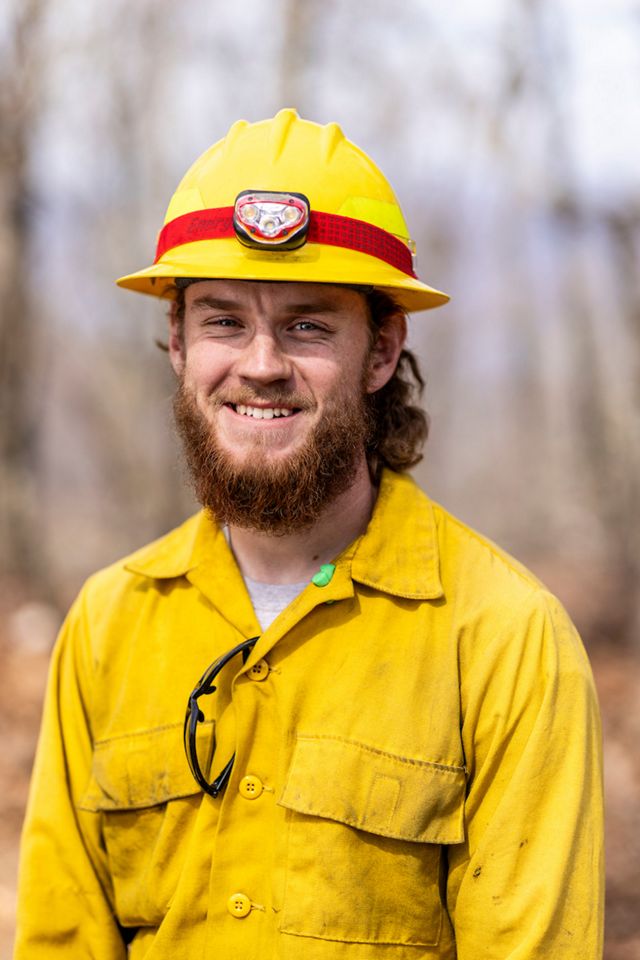 A smiling man stands in a yellow hard hat and yellow shirt.