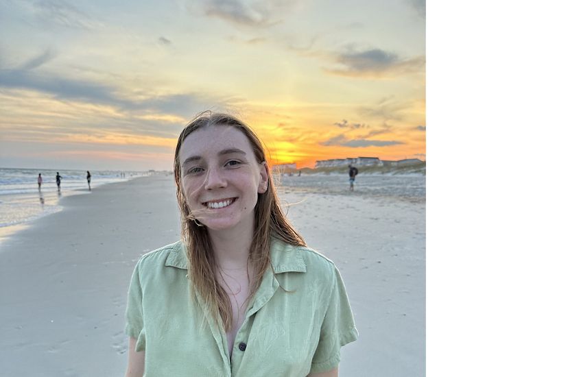 Candid headshot of Charlotte Welsby smiling in front of a sunset on the beach.