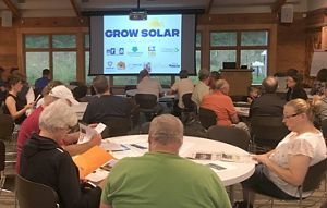 Photo of people sitting at tables during a presentation about solar electricity in Iowa.