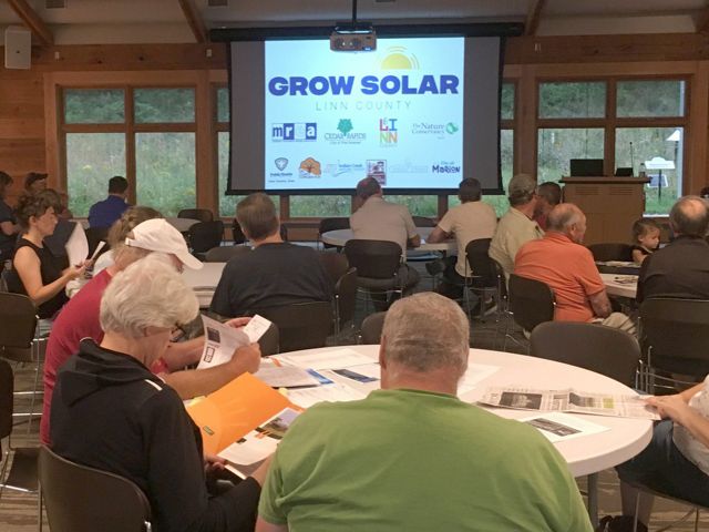 Photo of people sitting at tables during a presentation about solar electricity in Iowa.