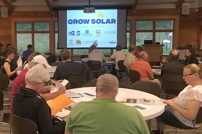 Photo of people sitting at tables during a presentation about solar electricity in Iowa.