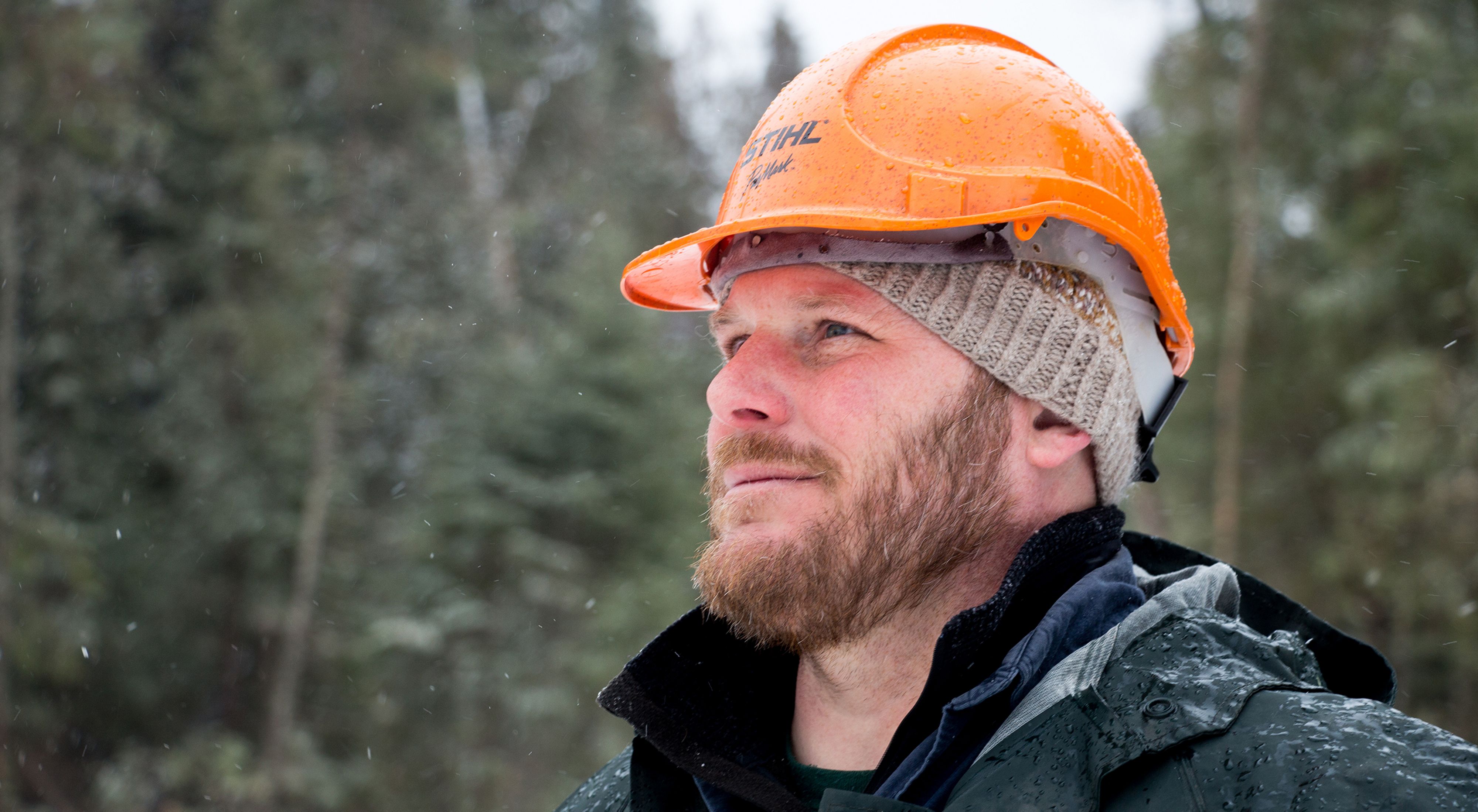 A close view of Chris Stone in the woods wearing a hard hat over a winter cap.