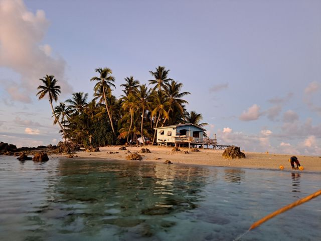 An idyllic island with a raised home. A person bends over in front of the water.