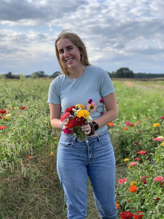 Photo of Colleen Stroud smiling while holding flowers in a field of colorful flowers.