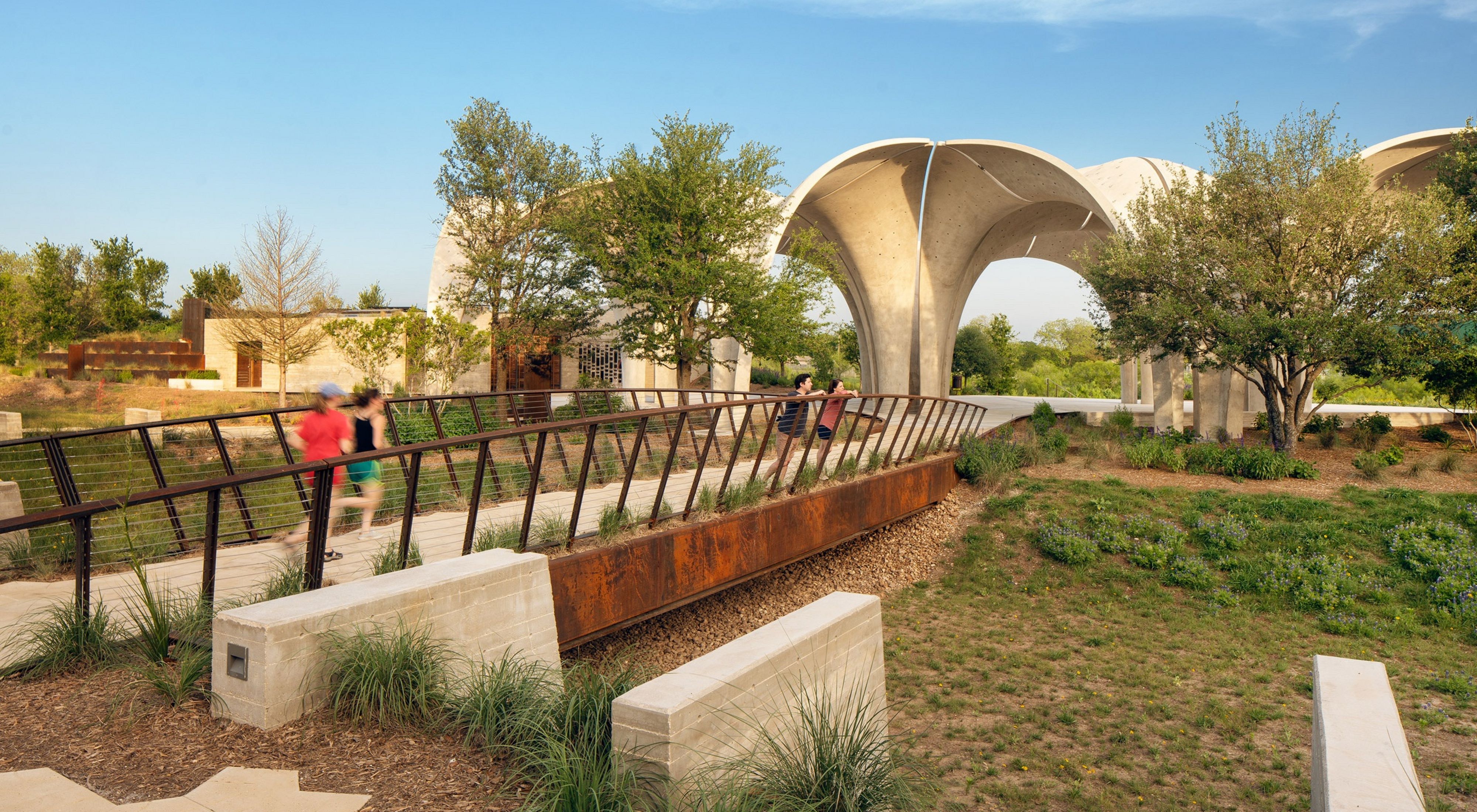 Four people explore a green park with a bridge and a limestone structure in the center.