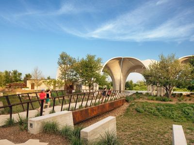 Four people explore a green park with a bridge and a limestone structure in the center.